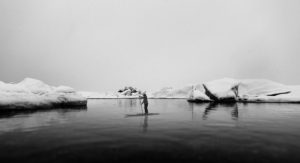 Black and white picture of a woman on stand-up paddleboard in front of icebergs in the background